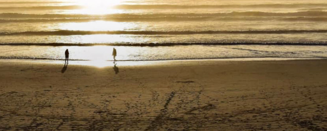 Sunset over the Washington coast with two people walking along the shoreline.